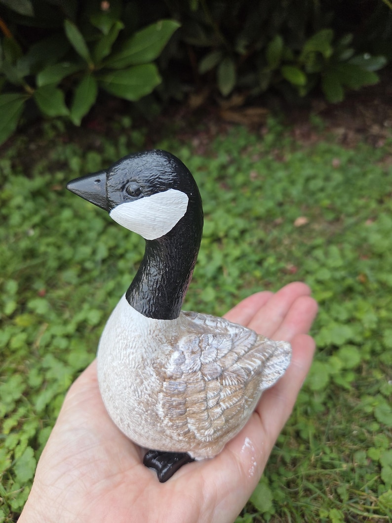 K&ouml;nnte beinhalten: Eine handbemalte G&auml;nsefigur mit schwarzem Kopf und Hals, einem wei&szlig;en Wangenfleck und einem beigefarbenen K&ouml;rper mit detaillierten Federmustern. Die Gans hat schwarze F&uuml;&szlig;e und einen schwarzen Schnabel. Die Figur wird in der Hand einer Person gehalten.