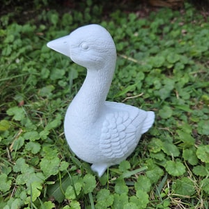 K&ouml;nnte beinhalten: Hellblaue G&auml;nsefigur mit detaillierten Federn und Augen. Die Gans steht auf gr&uuml;nem Gras und Klee. Die Figur hat einen gebogenen Hals und einen spitzen Schnabel, geeignet f&uuml;r Garten- oder Heimdekoration.