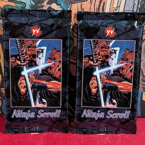 May include: Two identical rectangular trading card booster packs featuring the Ninja Scroll anime artwork. Each pack displays a character holding a katana with a glowing blue blade, the Yamato Cards logo at the top, and the text Ninja Scroll below.