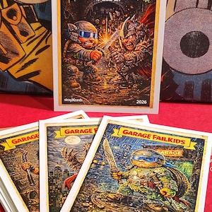 May include: A collection of "Garage Fail Kids" trading cards. The top card features two armored figures battling, with the text "Sewer Garage Fail Kids" and "10-Card Set." Other cards show cartoon characters with weapons. The cards are on a red surface.
