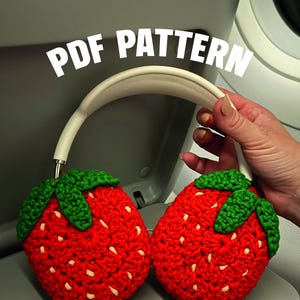 Könnte beinhalten: Kopfhörer mit roten, gehäkelten Erdbeer-Ohrmuscheln und einem weißen Bügel. Die Erdbeer-Ohrmuscheln haben grüne Blätter und weiße Samen. Der Text "PDF PATTERN" wird in weißen Buchstaben angezeigt.