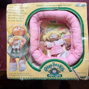 May include: Vintage Cabbage Patch Kids Pin-Ups doll set in original packaging. The box features a doll with blonde pigtails and a pink polka-dot bed frame. The text on the box reads "A friend for you and your Cabbage Patch Kid."