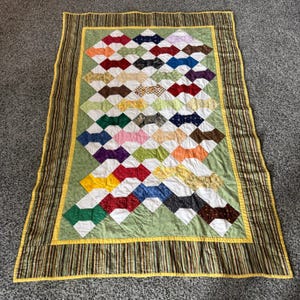 May include: A handmade quilt with a colorful diamond pattern. The quilt features a variety of fabrics in shades of red, yellow, green, blue, and brown. The quilt is bordered with a striped fabric and a yellow trim.