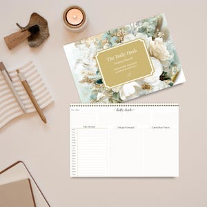 May include: A desktop planner with a floral design and the text "The Daily Dash." The planner includes sections for a daily schedule, notes, and goals. A candle, pens, and a decorative object are also visible.