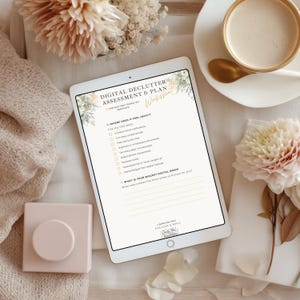 May include: A white tablet displaying a "Digital Declutter Assessment & Plan" worksheet. The worksheet includes checkboxes and prompts about digital organization. A cup of coffee and flowers are in the background.
