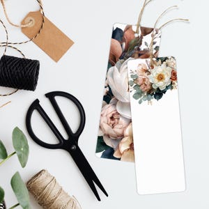 May include: Two floral bookmarks with watercolor flower designs, featuring white, pink, and peach roses. A black pair of scissors, twine, and a blank tag are also visible, suggesting a craft or gift theme.
