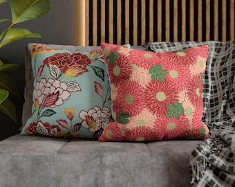 Könnte beinhalten: Zwei dekorative Zierkissen mit Blumenmustern auf einem grauen Sofa. Ein Kissen hat einen hellblauen Hintergrund mit roten, gelben und weißen Blumen. Das andere hat ein rotes Blumenmuster.