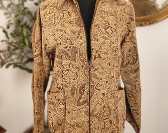 Pode incluir: Casaco com estampa paisley marrom e bege com zíper total e dois bolsos frontais. O casaco é exibido em um manequim preto com um colar de corrente dourada. Gola.