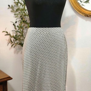 May include: A black mannequin torso is adorned with a gold chain necklace. The mannequin is wearing a black and white patterned pencil skirt. The skirt has a geometric design. A gold-framed mirror is in the background.