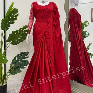 Może przedstawiać: Żywe czerwone sari prezentowane na manekinie. Sari ma skomplikowane hafty wzdłuż brzegów i rękawów, z pasującą bluzką. Materiał układa się elegancko, prezentując wzór. Widoczny jest tekst "Tithi Enterprise".