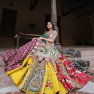 Puede incluir: Conjunto tradicional multicolor vibrante de falda y top. La falda presenta una base amarilla con intrincados bordados, paneles rojos y morados y espejos decorativos. El top está adornado con bordados detallados y una bufanda verde.