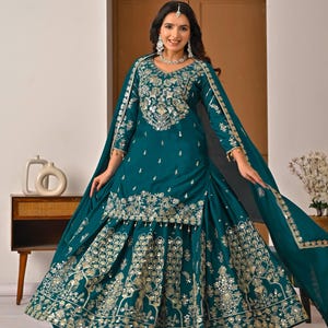 Puede incluir: Vestido formal bordado de color turquesa con detalles dorados. El vestido presenta intrincados patrones en el corpiño, las mangas y la falda. Un chal a juego cae sobre los hombros. El conjunto incluye un tocado y joyas a juego.