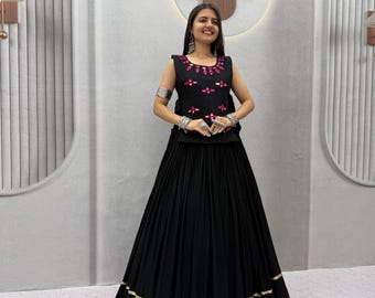 May include: A black sleeveless top featuring a round neckline with pink mirror embellishments and a matching black floor-length skirt with a gold-toned border at the hem. The ensemble includes silver-toned bangles and earrings as accessories.