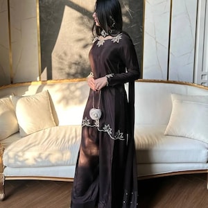 May include: A dark brown long-sleeved tunic and wide-leg trousers set featuring white floral embroidery along the neckline and hem. The outfit includes a matching scarf with white embellishments and a small, round, silver-toned metallic handbag.