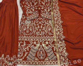 Puede incluir: Conjunto salwar kameez bordado de color óxido con pantalón y dupatta a juego. El conjunto presenta intrincados trabajos de hilo de oro y plata, incluidos motivos de pavo real. Zapatos negros y dorados adornados completan el look.
