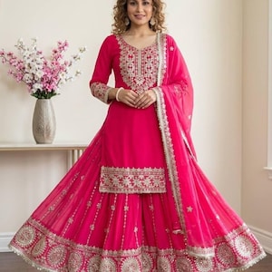 Puede incluir: Un vibrante conjunto de salwar kameez fucsia. El atuendo presenta intrincados bordados dorados en el escote, el corpiño y el dobladillo de la falda acampanada. Una dupatta a juego con un delicado borde completa el look. El atuendo se usa con zapatos a juego.
