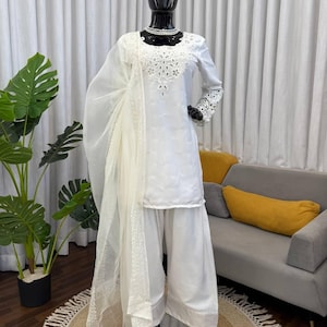 May include: A white ceramic mug with a black handle and the text "But First, Coffee" in a black, handwritten-style font. The mug is on a white surface.