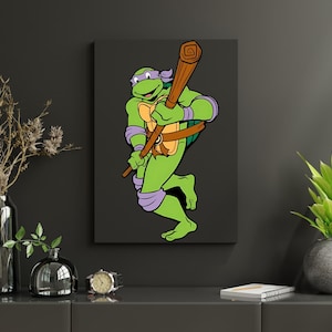 May include: A canvas print featuring a cartoon image of a green turtle-like character holding a wooden staff. The character is wearing a purple mask and arm and leg bands. The background is a solid dark gray.
