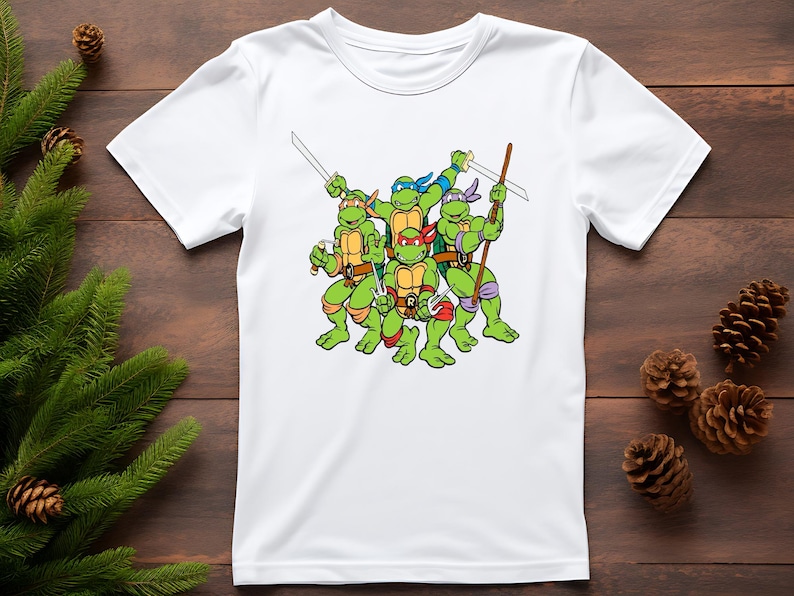 May include: White t-shirt featuring a graphic of the Teenage Mutant Ninja Turtles. The turtles are green with colored masks and holding weapons. The design is centered on the shirt.