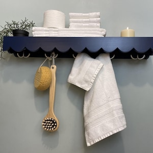 May include: A navy blue shelf with scalloped edges and silver hooks. The shelf is decorated with towels, a candle, a sponge, and a wooden body brush.