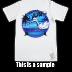 以下が含まれることがあります： 白いTシャツ。青と白の海の波のデザインとヤシの木のシルエットが特徴です。「Tasha」の文字が波の上に書かれています。「This is a sample」の文字がTシャツの下部に印刷されています。