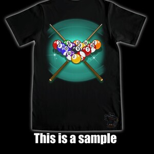 May include: Black t-shirt featuring a graphic of a rack of billiard balls with crossed pool cues. The balls are numbered and arranged in a triangle. The text "This is a sample" is at the bottom of the shirt.