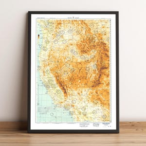 Może przedstawiać: Oprawiony wydruk mapy vintage zachodnich Stanów Zjednoczonych, z szczegółowym widokiem topograficznym w odcieniach brązu i beżu. Mapa jest w czarnej ramie, prezentowana na drewnianej powierzchni.