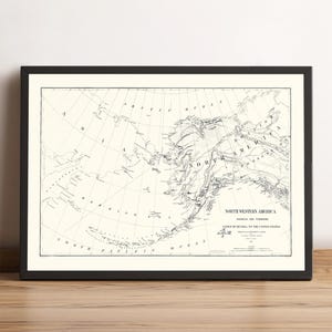 May include: Framed vintage map of North Western America, including Alaska, in black and white. The map shows the territory ceded by Russia to the United States. The map is in a black frame and is displayed on a wooden surface.