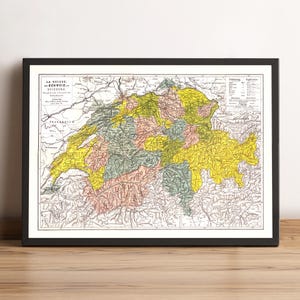 May include: Framed vintage map of Switzerland, featuring a detailed depiction of the country's regions in shades of yellow, green, and pink. The map is encased in a black frame, resting on a wooden surface.