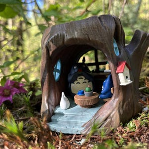Op de afbeelding: Een handgeschilderde miniatuur boomhut sc&egrave;ne met een Totoro figuur, een kleine tafel met een cactus en een vogelhuisje. Het boomhuis is bruin met blauwe raamkozijnen en een lichtblauwe basis, te midden van groen.