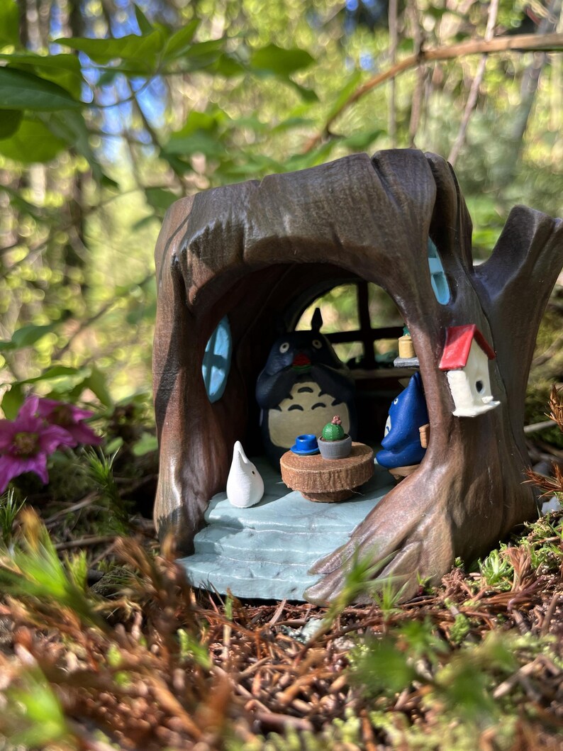 Op de afbeelding: Een handgeschilderde miniatuur boomhut sc&egrave;ne met een Totoro figuur, een kleine tafel met een cactus en een vogelhuisje. Het boomhuis is bruin met blauwe raamkozijnen en een lichtblauwe basis, te midden van groen.