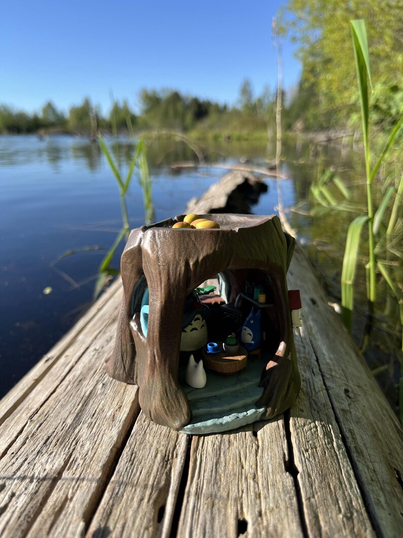 Op de afbeelding: Een gedetailleerd miniatuur boomstronk diorama met personages uit een populaire animatiefilm. De bruine hars sculptuur heeft een blauw interieur met kleine figuren en een tafel. Het diorama staat op een verweerde houten stam.
