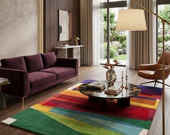 May include: A rectangular area rug featuring a geometric pattern of bold, overlapping color blocks in shades of green, blue, yellow, red, and purple, laid out on a dark wood floor in a living room setting with a dark purple sofa and coffee table.