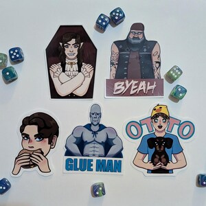 May include: Five die-cut stickers featuring illustrated characters and the text BYEAH, GLUE MAN, and OTOTO, surrounded by scattered six-sided dice. The stickers depict a vampire, a bearded man, a person eating a burger, a muscular figure, and a person with a dog.