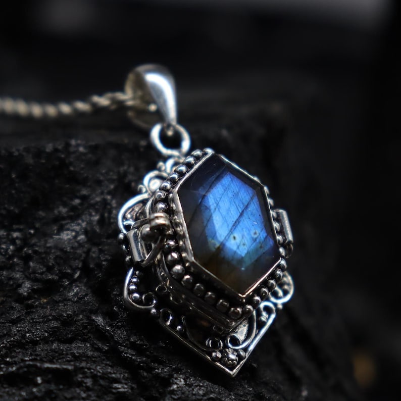 May include: A silver pendant necklace featuring a faceted, iridescent blue gemstone. The gemstone is set in an ornate, detailed silver setting with a decorative bail. The chain is a delicate silver link.