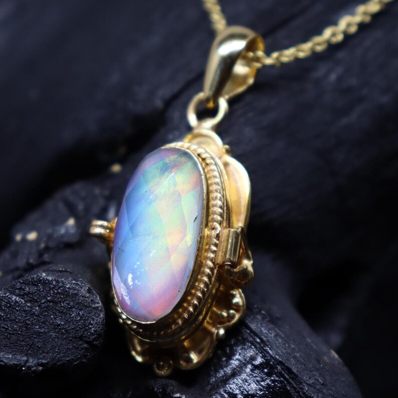 May include: A gold pendant necklace featuring an oval-shaped opal gemstone. The opal displays a range of colors, including blue, pink, and yellow. The pendant is set in a gold frame with intricate detailing, and hangs from a delicate gold chain.