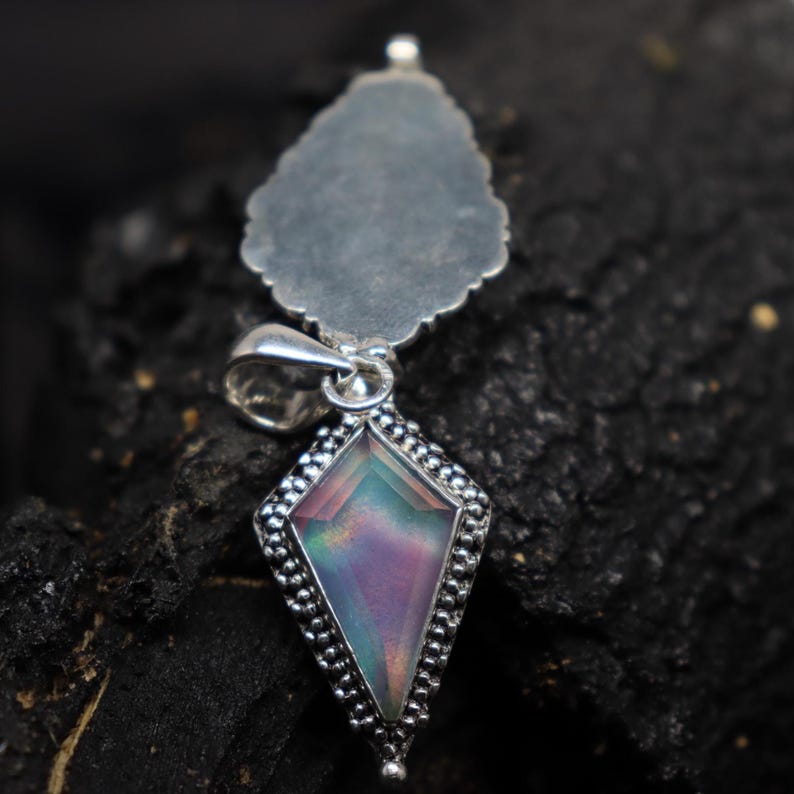 Pu&ograve; includere: Ciondolo in argento con una pietra preziosa iridescente a forma di aquilone. La pietra mostra una gamma di colori, tra cui rosa, viola e verde. Il ciondolo ha un bordo dettagliato con perline e un retro pi&ugrave; grande a forma di foglia.
