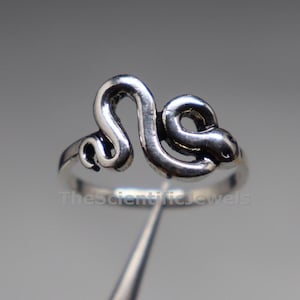 May include: A silver-toned ring featuring a coiled snake design that forms the centrepiece of the band. The metal has a polished finish with darkened recessed areas to define the serpent's body and head. The text TheScientificJewels is visible.