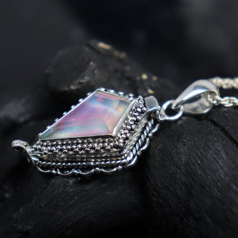 Pu&ograve; includere: Una collana con pendente in argento con una gemma triangolare iridescente. La gemma mostra sfumature di rosa, viola e verde. Il pendente ha un'incastonatura in argento dettagliata e ornata con un bordo decorativo.