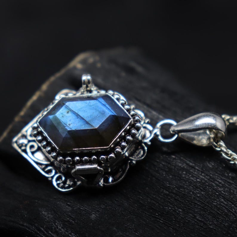 May include: A silver pendant necklace featuring a faceted, blue gemstone. The gemstone is set in an ornate, detailed silver setting with a decorative bail. The chain is a delicate silver link.