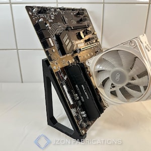 Può includere: Un supporto per componenti per computer in metallo nero che tiene una scheda madre e un dissipatore CPU bianco con una ventola. La scheda madre ha vari componenti e il testo "MSI". Il dissipatore ha una grande ventola.