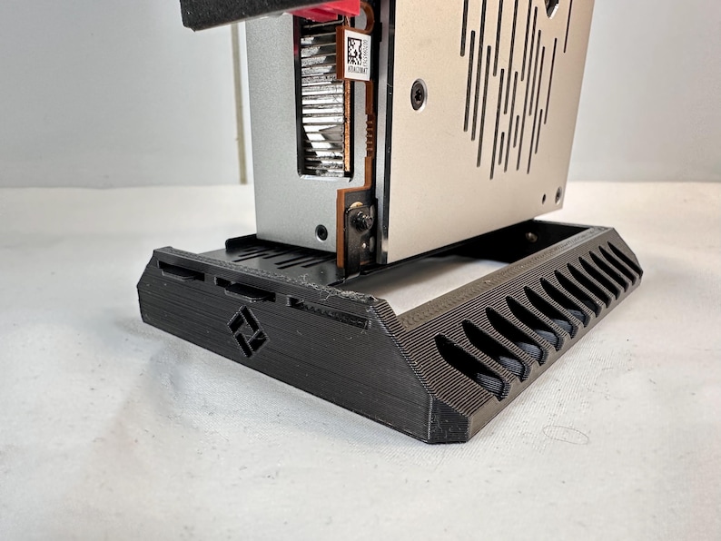 K&ouml;nnte beinhalten: Ein schwarzer, 3D-gedruckter Computerkomponentenst&auml;nder mit geometrischem Design. Der St&auml;nder tr&auml;gt eine silberne und schwarze Computerkomponente mit sichtbarem rotem Licht. Der St&auml;nder hat eine Reihe von abgewinkelten Schlitzen.