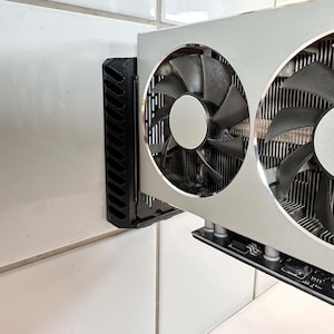 K&ouml;nnte beinhalten: Eine silberne und schwarze Computer-Grafikkarte mit zwei gro&szlig;en L&uuml;ftern. Die L&uuml;fter haben schwarze Fl&uuml;gel und sind in einem silbernen Geh&auml;use untergebracht. Eine schwarze Halterung ist zur Montage an der Seite angebracht.