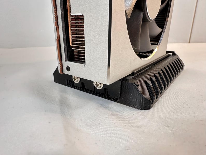 K&ouml;nnte beinhalten: Eine silberne und schwarze Computer-Grafikkarte mit einem L&uuml;fter. Die Karte hat eine schwarze Basis mit einem geriffelten Design. Der L&uuml;fter ist schwarz und silber, und die Karte hat Kupferk&uuml;hlk&ouml;rper.