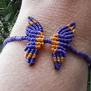 May include: A handmade macrame bracelet featuring a butterfly design. The butterfly wings are a combination of blue and yellow, with a matching blue band. The bracelet is designed to be worn on the wrist.