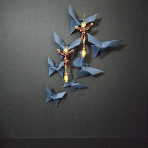 Pode incluir: Brincos de borboleta origami azul marinho com detalhes dourados e contas amarelas penduradas. Os brincos são combinados com várias borboletas de origami em vários tamanhos, criando uma exibição artística única.
