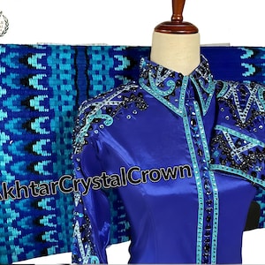 Könnte beinhalten: Ein königsblaues Reitturniershirt mit türkisfarbenen und schwarzen Verzierungen. Das Shirt hat lange Ärmel und wird auf einer Schaufensterpuppe präsentiert. Eine blaue gemusterte Decke befindet sich hinter dem Shirt. Der Text "Akhtar Crystal Crown" ist sichtbar.