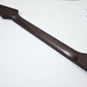 May include: A dark brown guitar neck with a headstock featuring six tuning peg holes. The neck is made of wood and has a smooth, polished finish. The logo for 3 Hit Guitars is in the upper right corner.