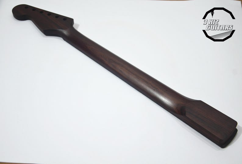 May include: A dark brown guitar neck with a headstock featuring six tuning peg holes. The neck is made of wood and has a smooth, polished finish. The logo for 3 Hit Guitars is in the upper right corner.