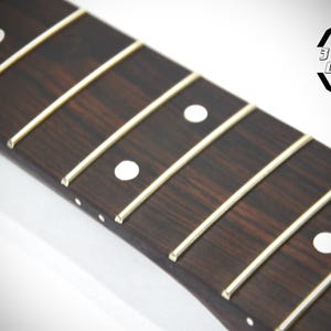 May include: Close-up of a guitar fretboard with dark brown wood and white fret markers. The frets are thin, light-colored metal. The logo "3 Kit Guitars" is in the upper right corner.